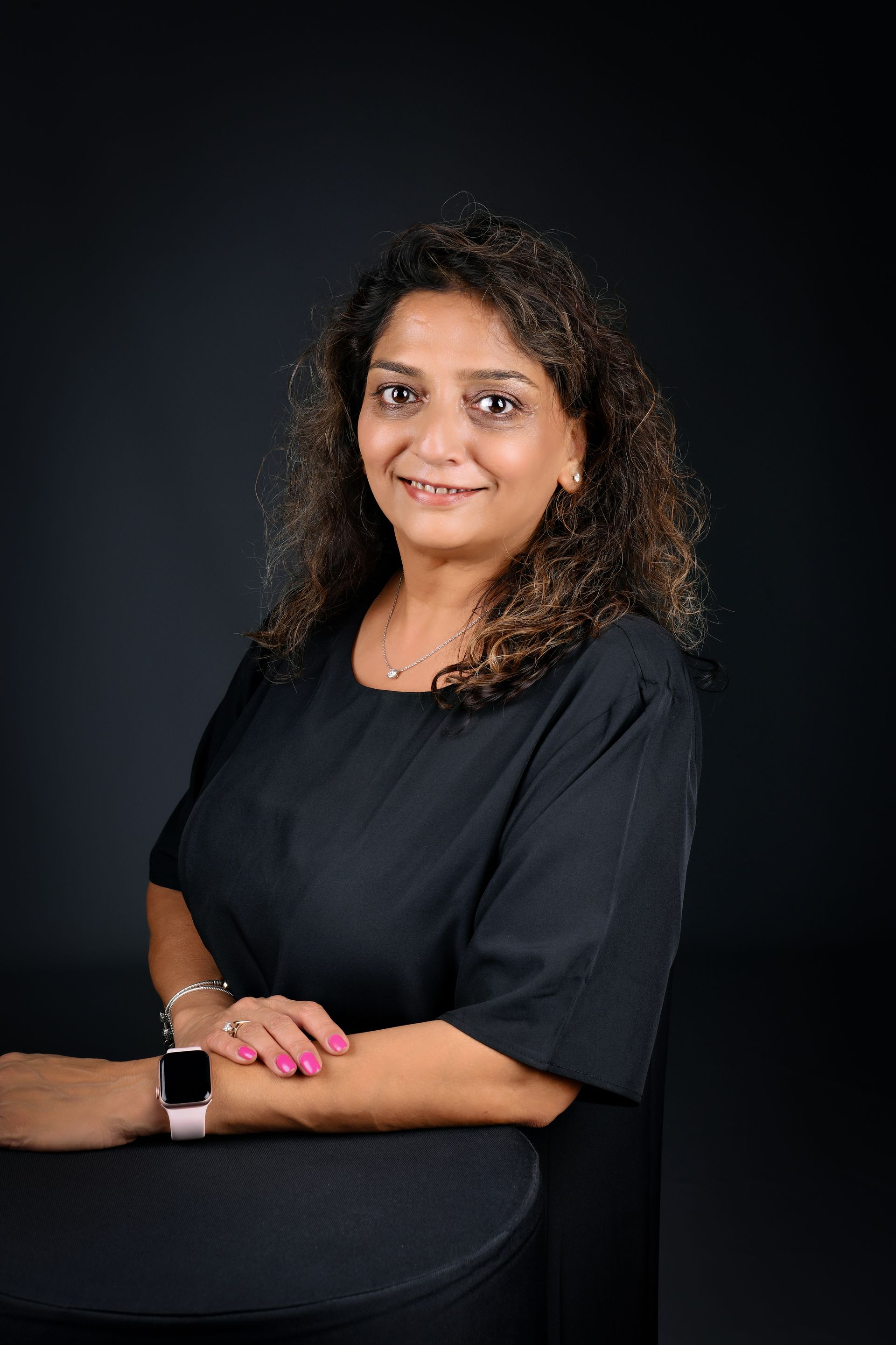 A woman is sitting at a desk with a laptop and a vase of flowers.