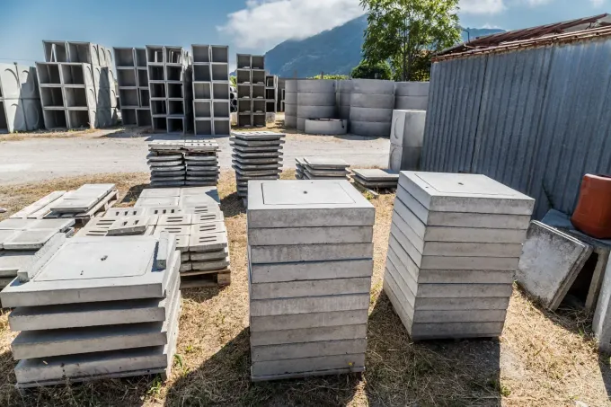 Pile di blocchi di cemento grigi in un cortile esterno accanto a un container metallico blu.