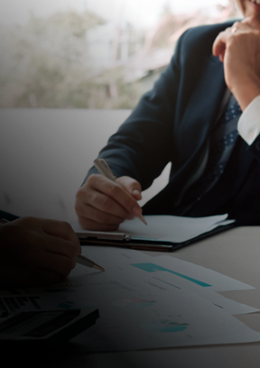 Um homem de terno e gravata está sentado à mesa escrevendo em uma prancheta.