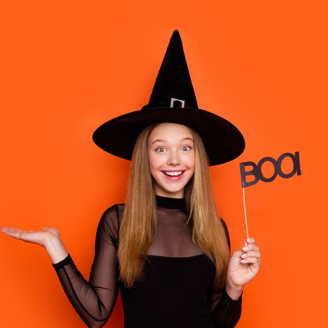 A woman in a witch costume is holding a sign that says boo