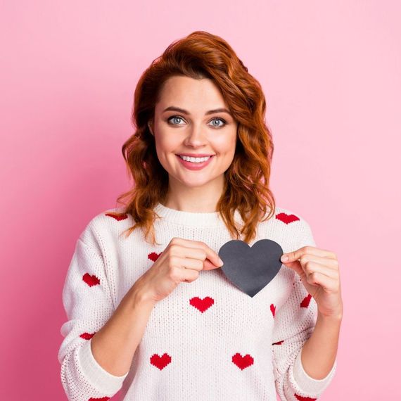 A woman in a white sweater with red hearts is holding a black heart.