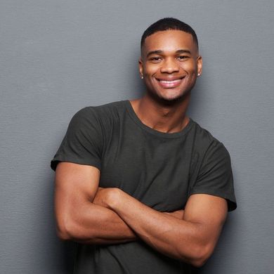 A man in a black shirt is smiling with his arms crossed