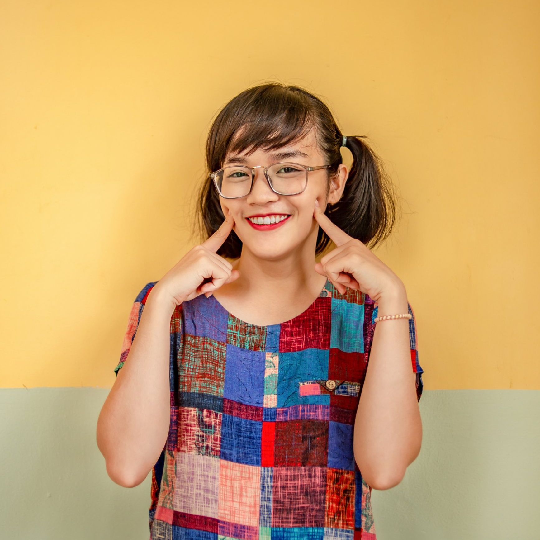 Woman with glasses and pigtails, pointing to her smile
