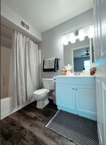 Bathroom with white walls, dark wood floor, white toilet, and shower curtain.