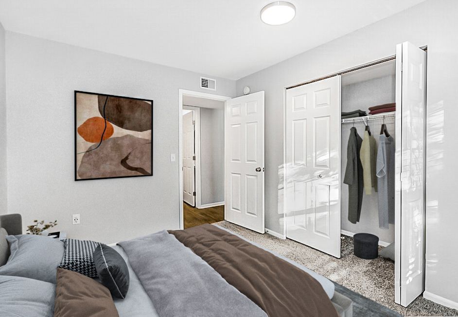 Bedroom with a bed, closet, art, and doorway. Walls are gray. Clothes hang inside the open closet.