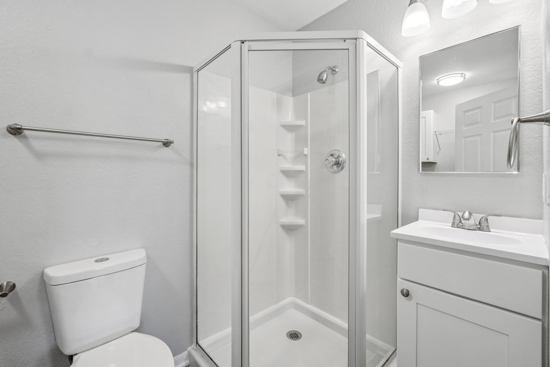 White bathroom with shower, toilet, and vanity. Gray walls and silver fixtures.