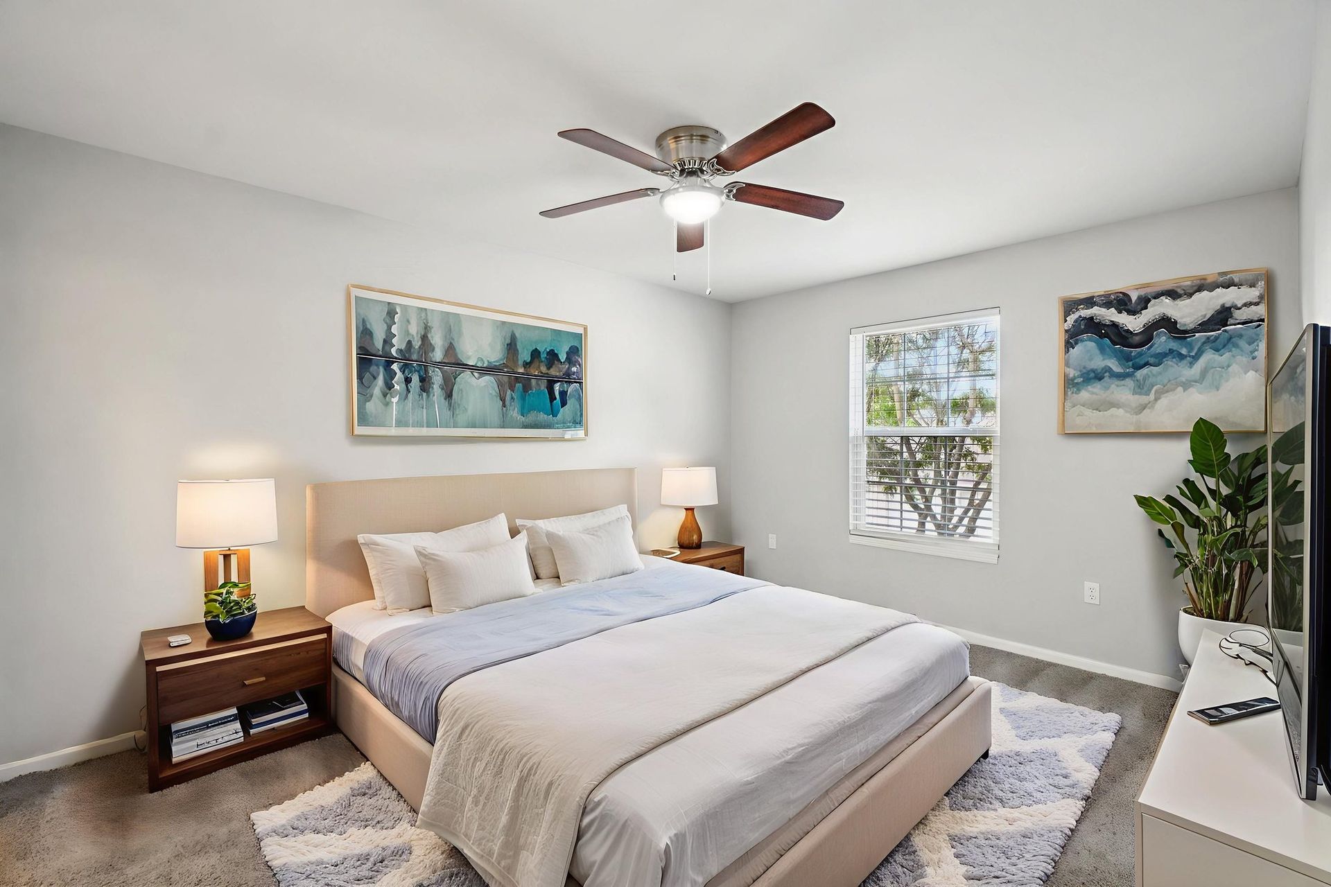 Bedroom with bed, nightstands, artwork, and window. Gray walls, light bedding, and a ceiling fan.
