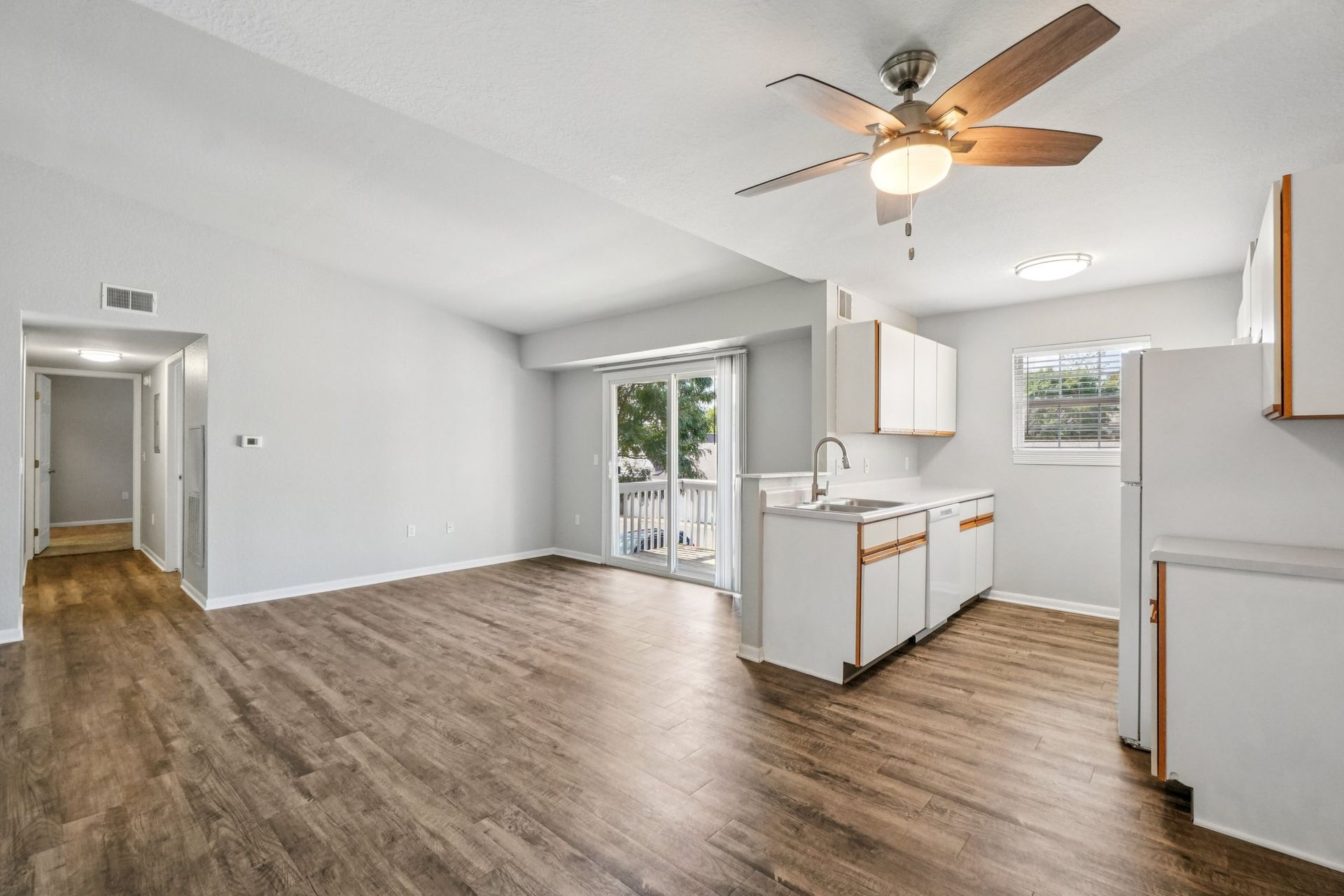 Empty apartment interior with kitchen, sliding doors, and wood-look flooring.