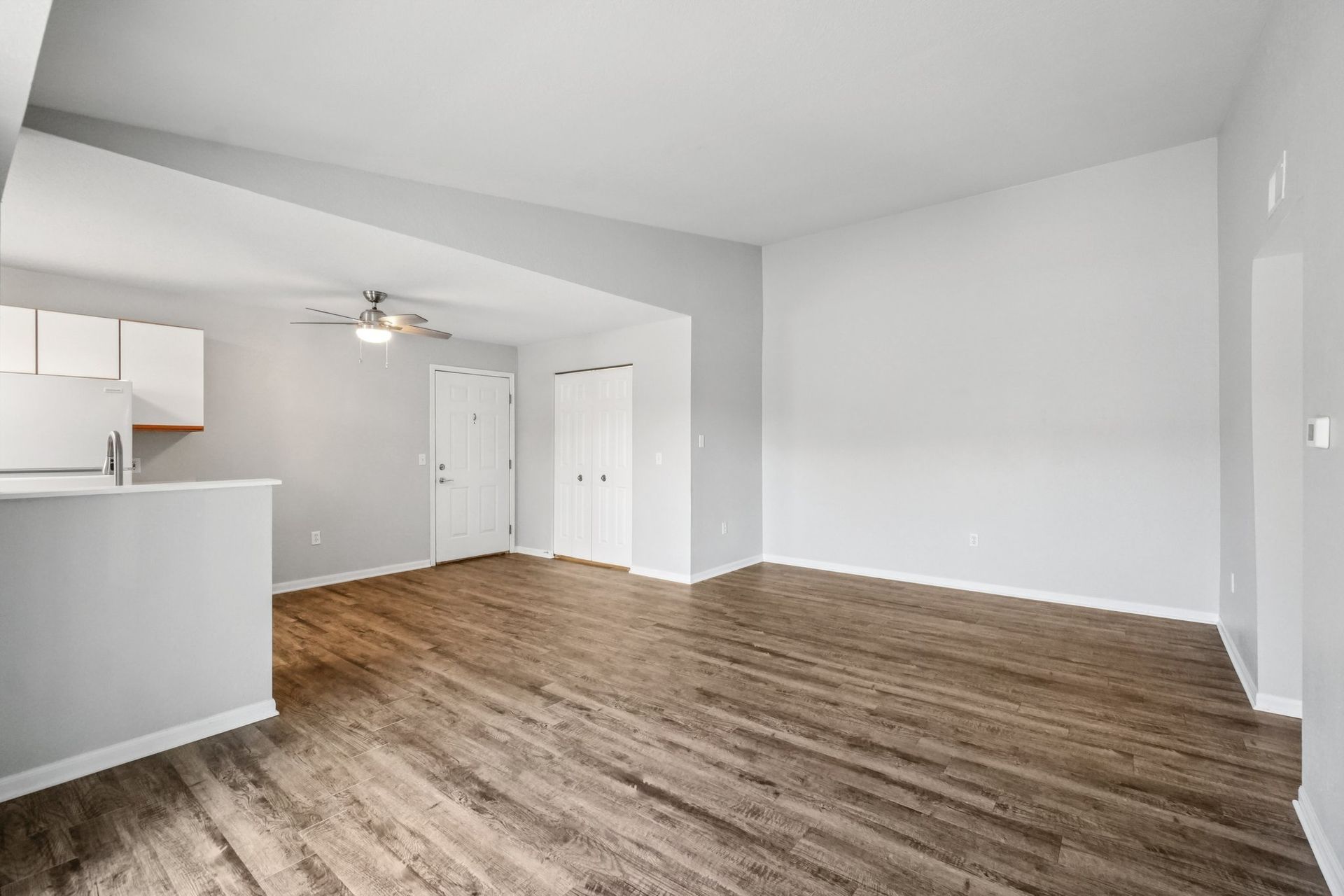 Empty living room with wood-look flooring, light gray walls, and white cabinets.