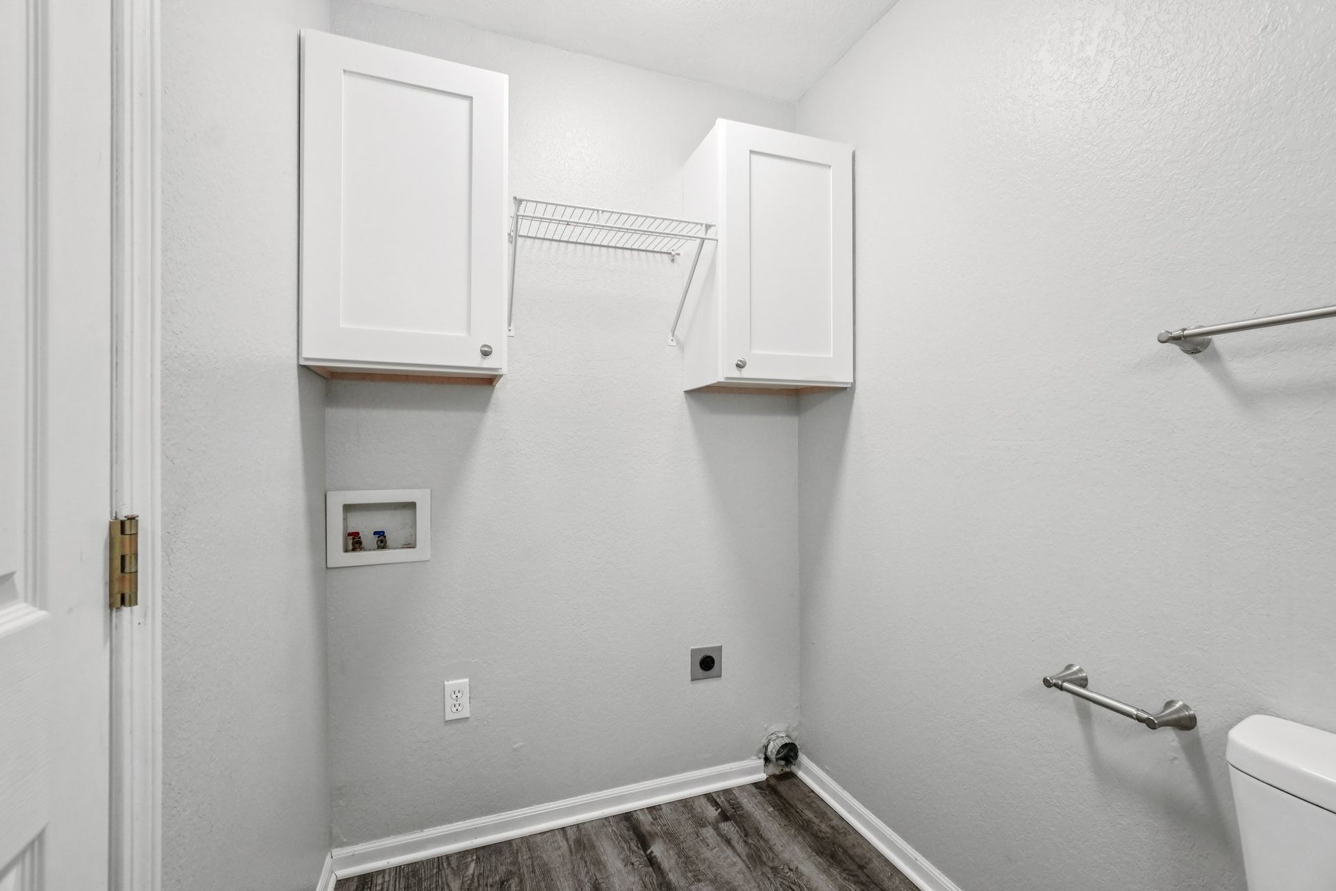 Laundry room with white cabinets, wire rack, and washing machine connections. Gray walls and flooring.