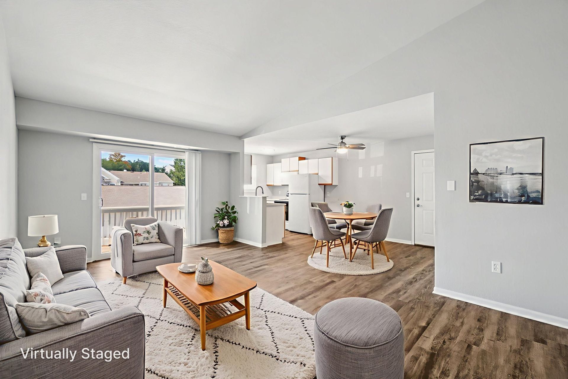 A staged interior of a living room with gray furniture, dining area, and a balcony.