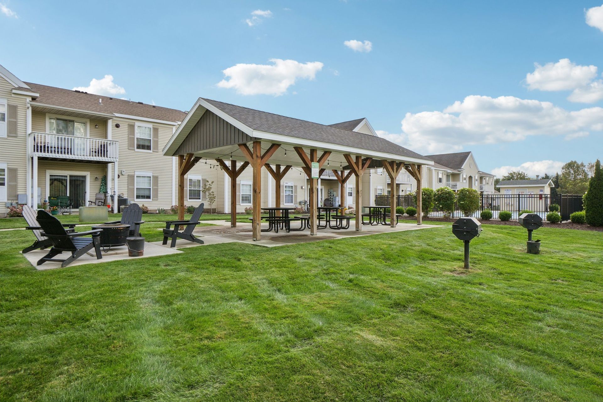 Grassy outdoor area with covered picnic tables, grills, and apartment buildings in the background.