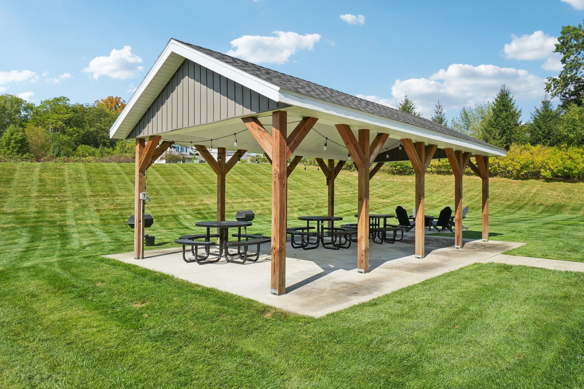 Picnic shelter with tables and benches on concrete, in grassy area.