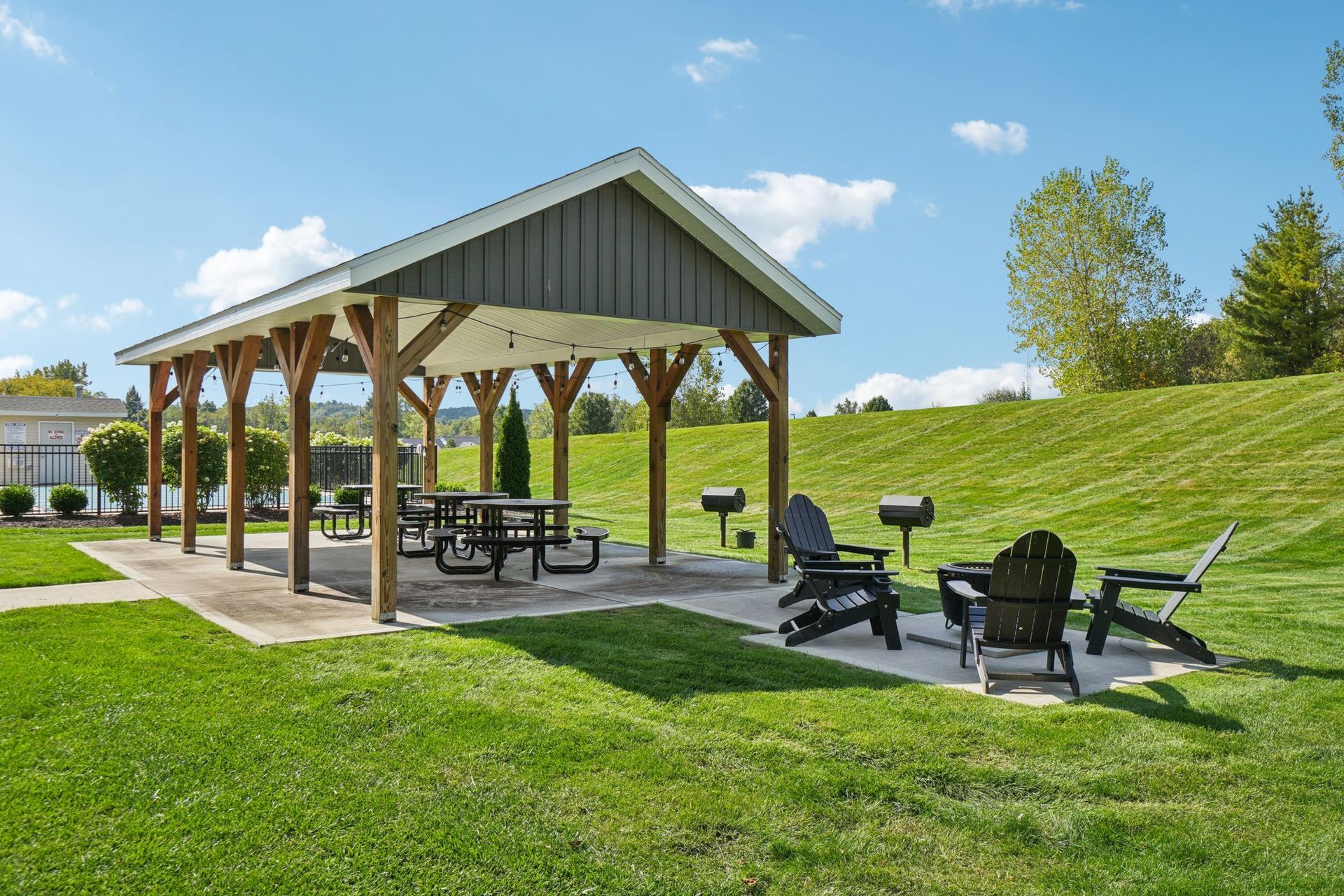 Picnic shelter with picnic table, chairs, and grills in a grassy area under a blue sky.