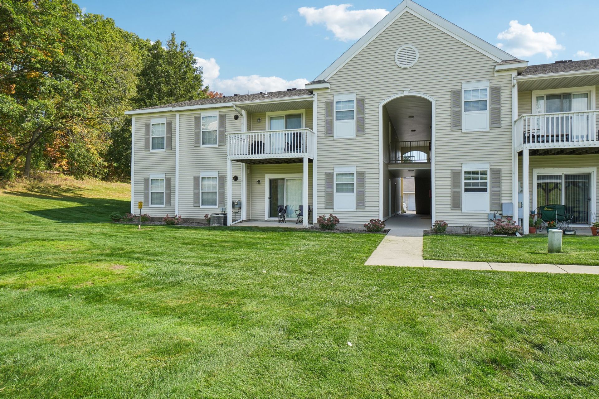Apartment building with beige siding, balconies, and a grassy lawn, under a bright sky.