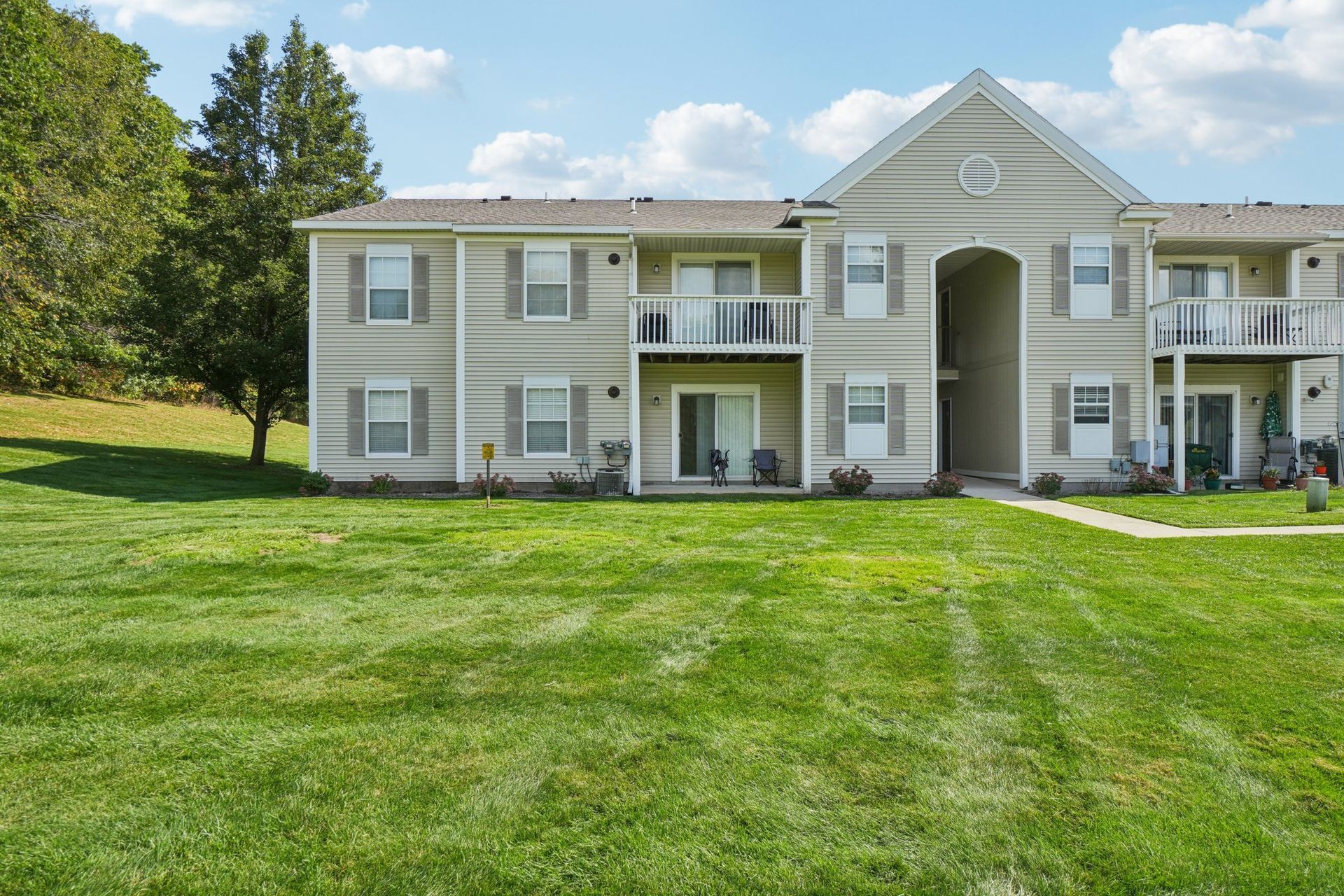 Light beige apartment building with balconies, set in grassy yard under blue sky.