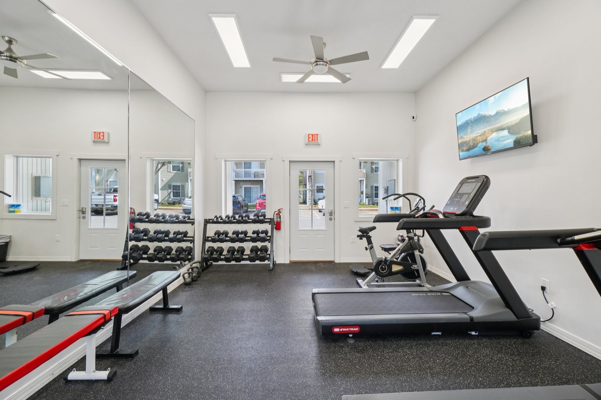 Gym interior with weights, treadmill, stationary bike, benches, and a TV.