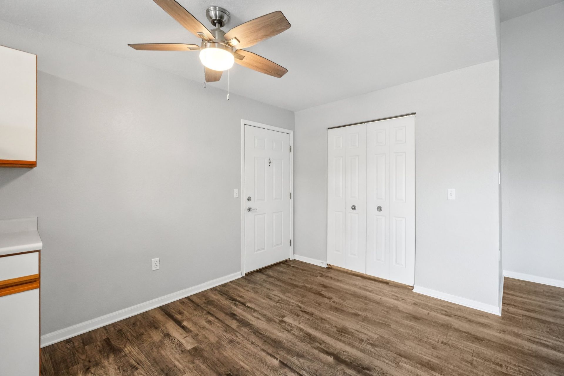 Empty room with wooden floors, white door, and closet. Ceiling fan with light.