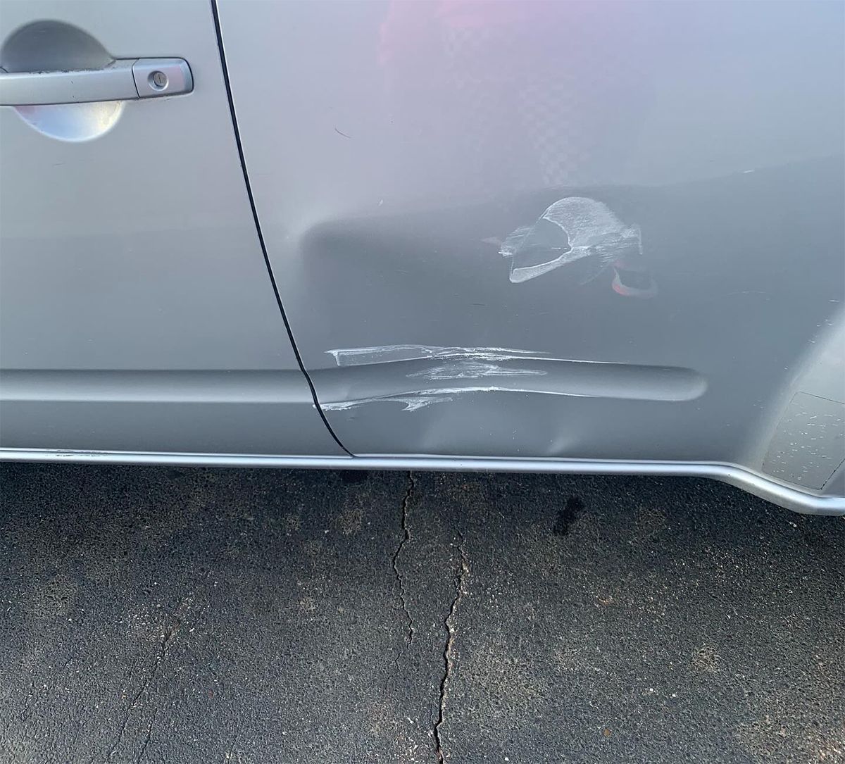 Silver car door with scratches and dents near the lower panel and side trim.
