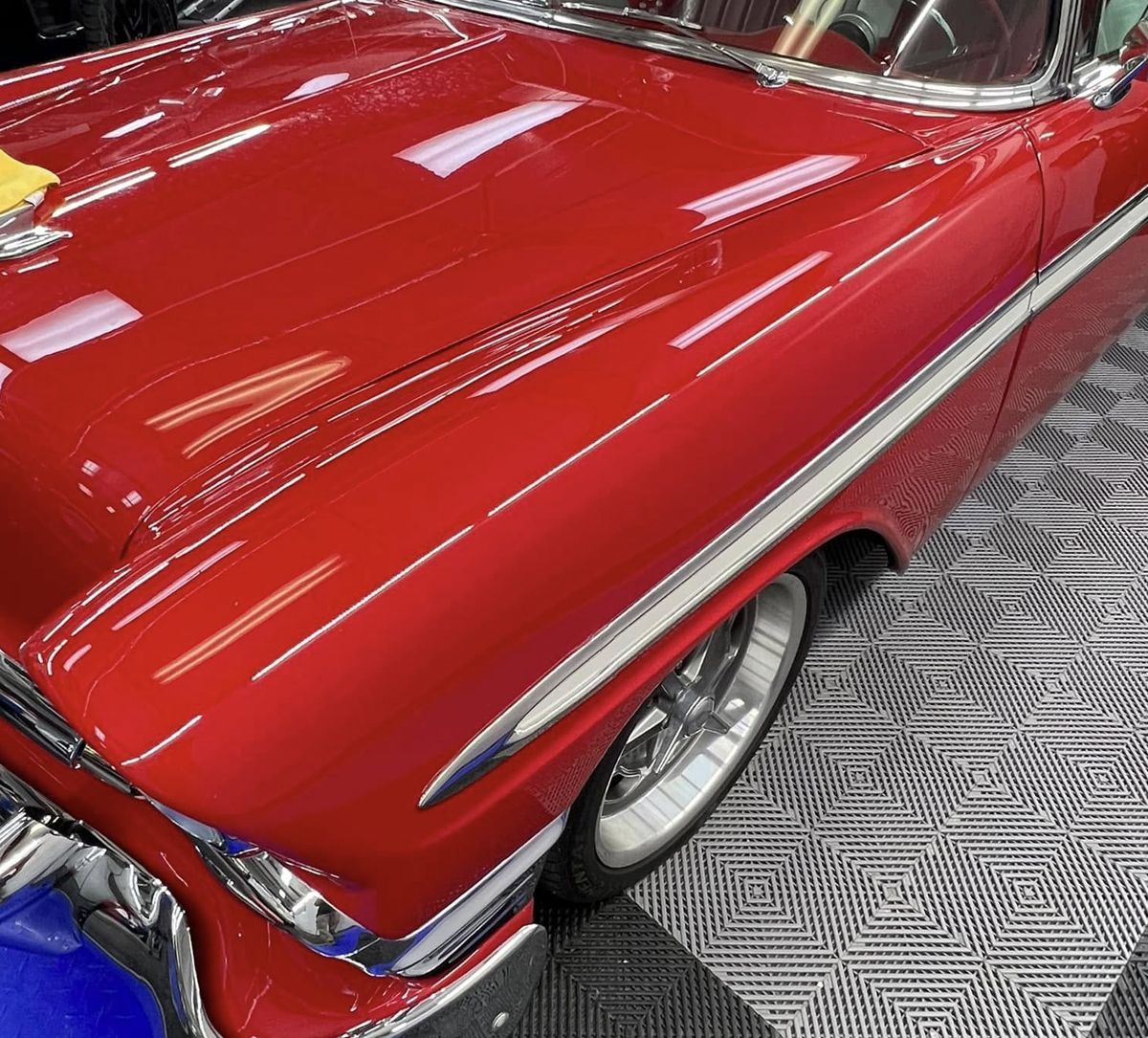 Shiny red classic car hood and front fender on a checkered showroom floor