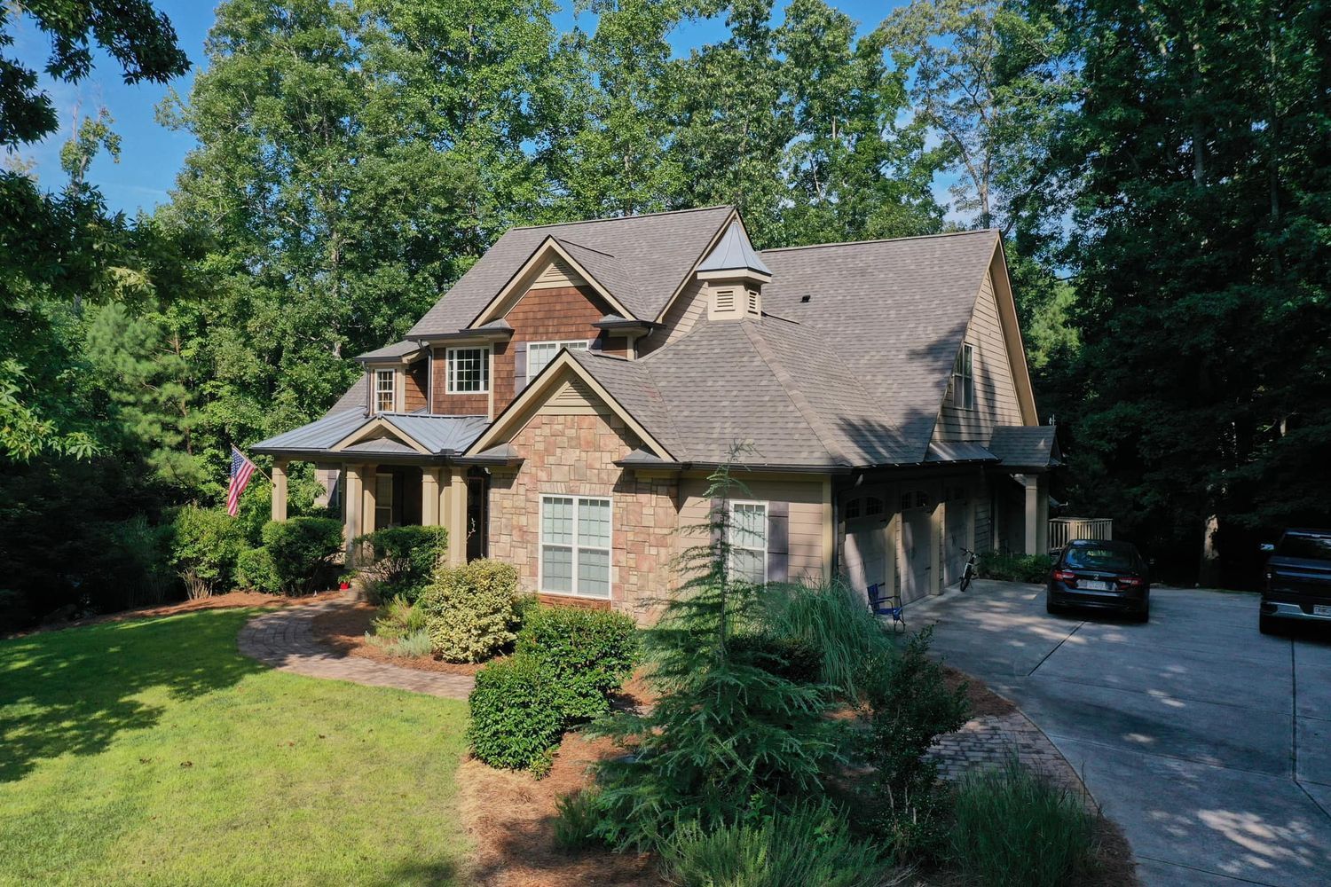Two-story house with brick and wood siding, asphalt shingle roof, surrounded by trees.
