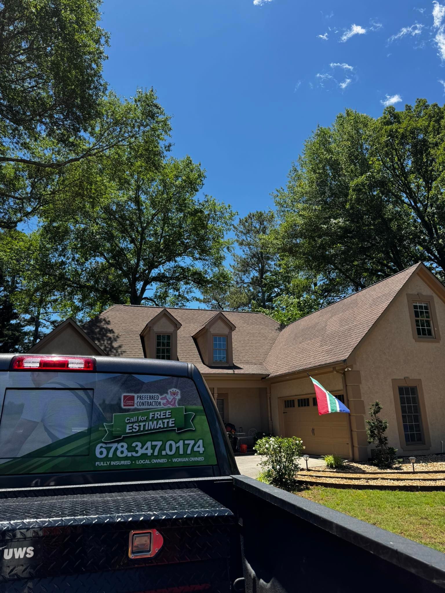 A house with a brown roof and a green and white company truck with a phone number in front.