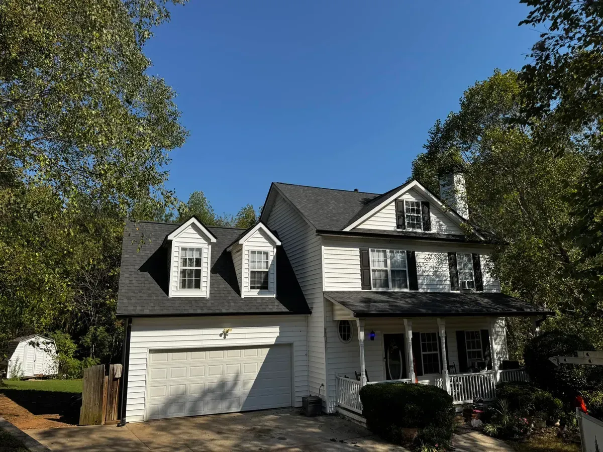 White two-story house with black shutters, white garage door, and a porch, set against a blue sky.