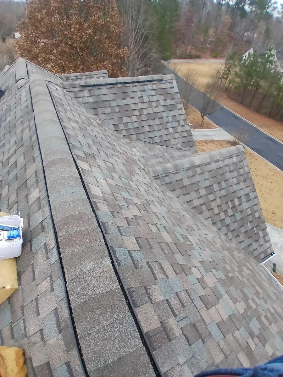 View of a multi-colored shingle roof with a ridge, boxes, and a driveway in the background.