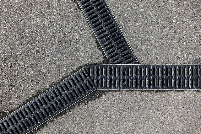 Three black drainage grates intersect on gray asphalt.
