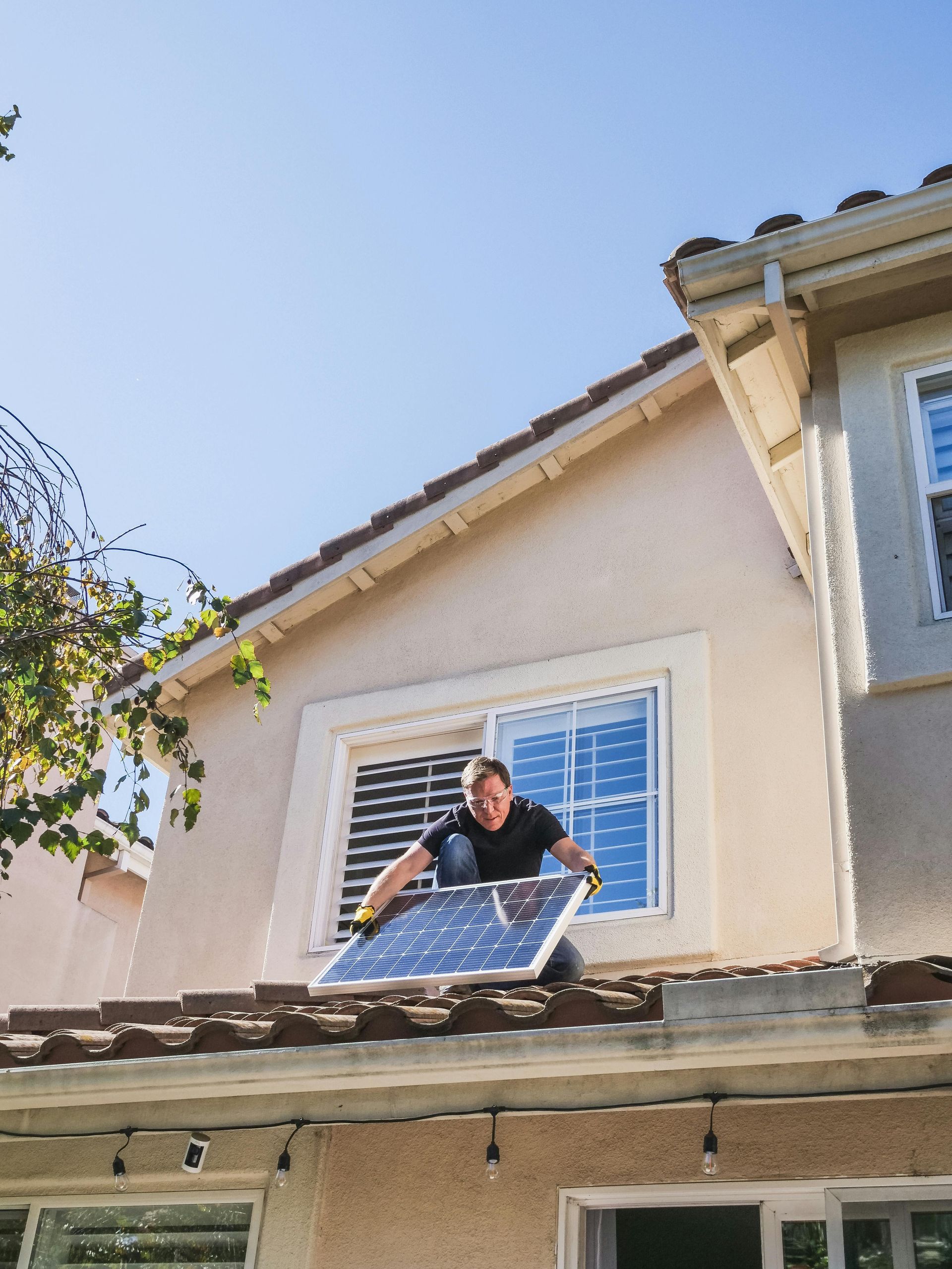 Man installing solar panel on a roof; sunny day. Beige house, blue sky.