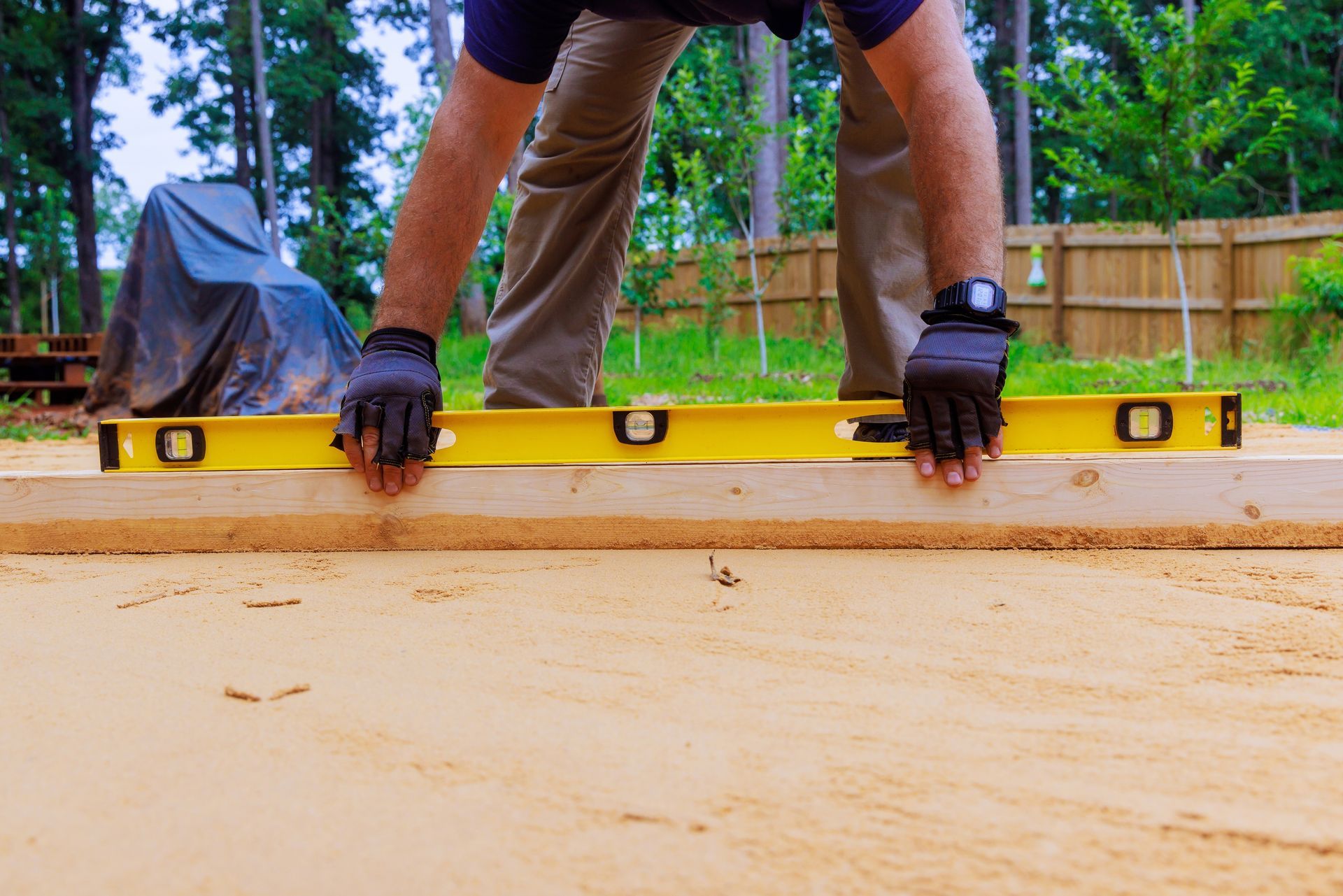 Person using a level on a wooden plank, outside.