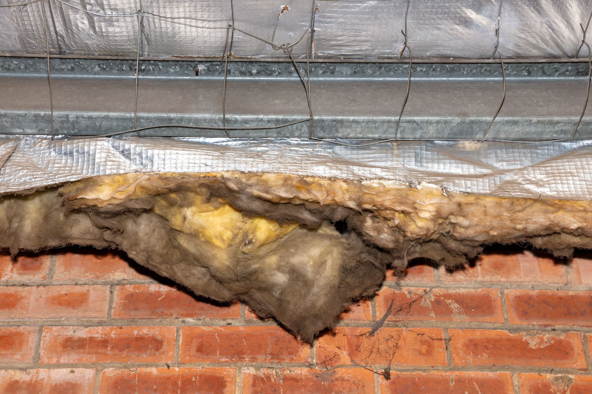 Exposed insulation and metal framing above a red brick wall.