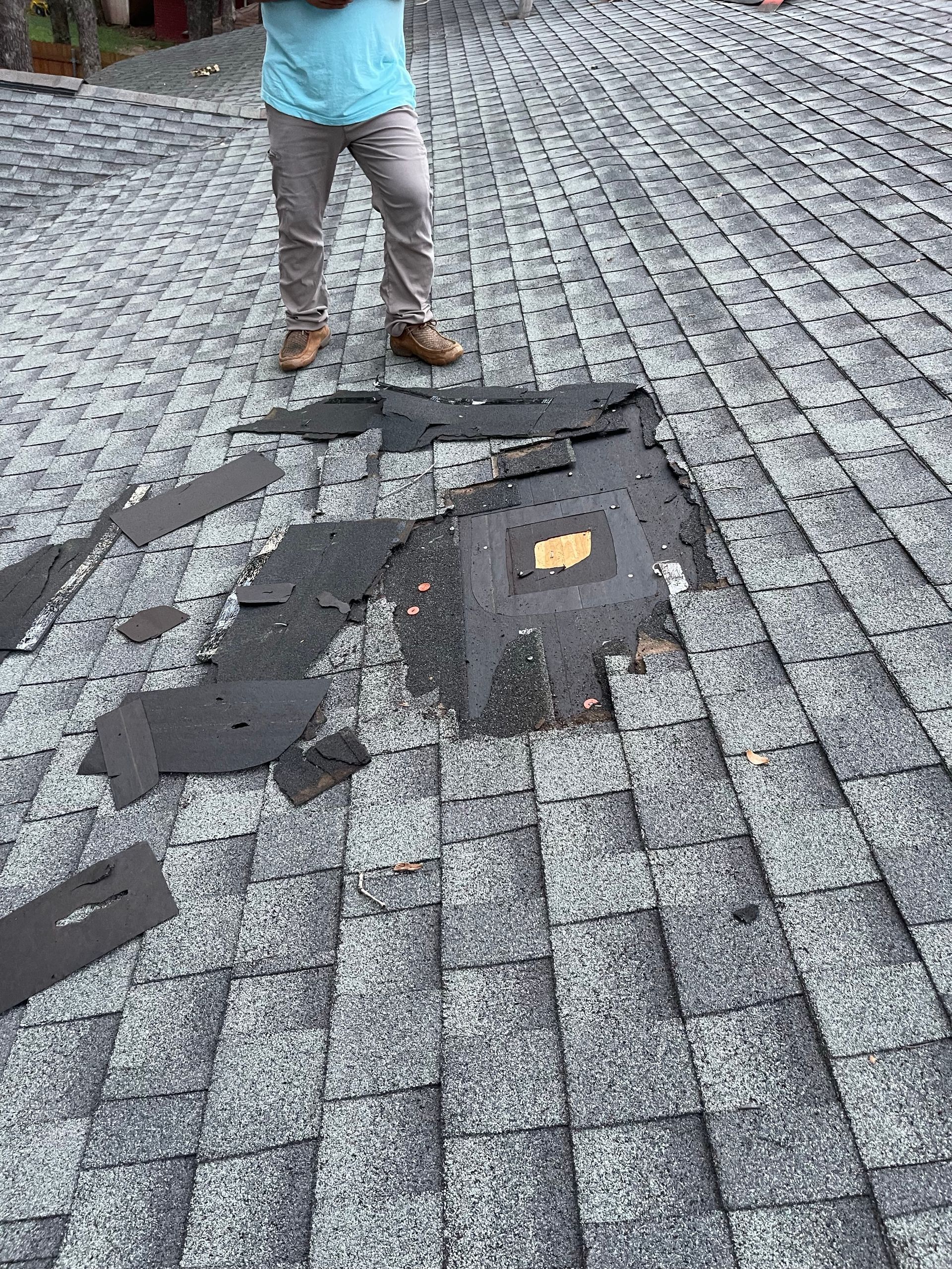 Person standing on a roof with a large area of missing shingles.