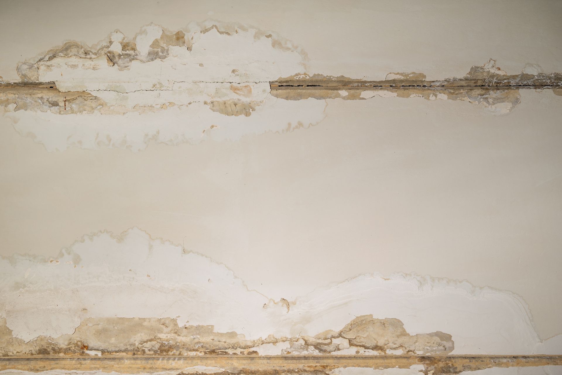 Water-damaged ceiling with peeling paint and exposed plaster, showing discoloration and moisture stains.