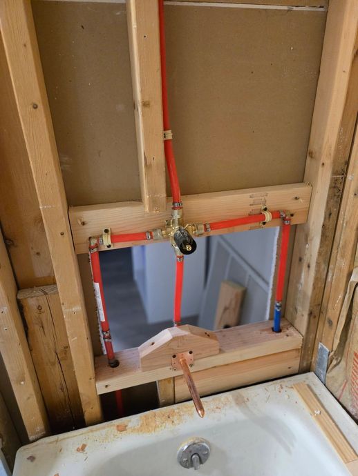 Bathroom wall under renovation with exposed framing and a rectangular cutout above a sink.