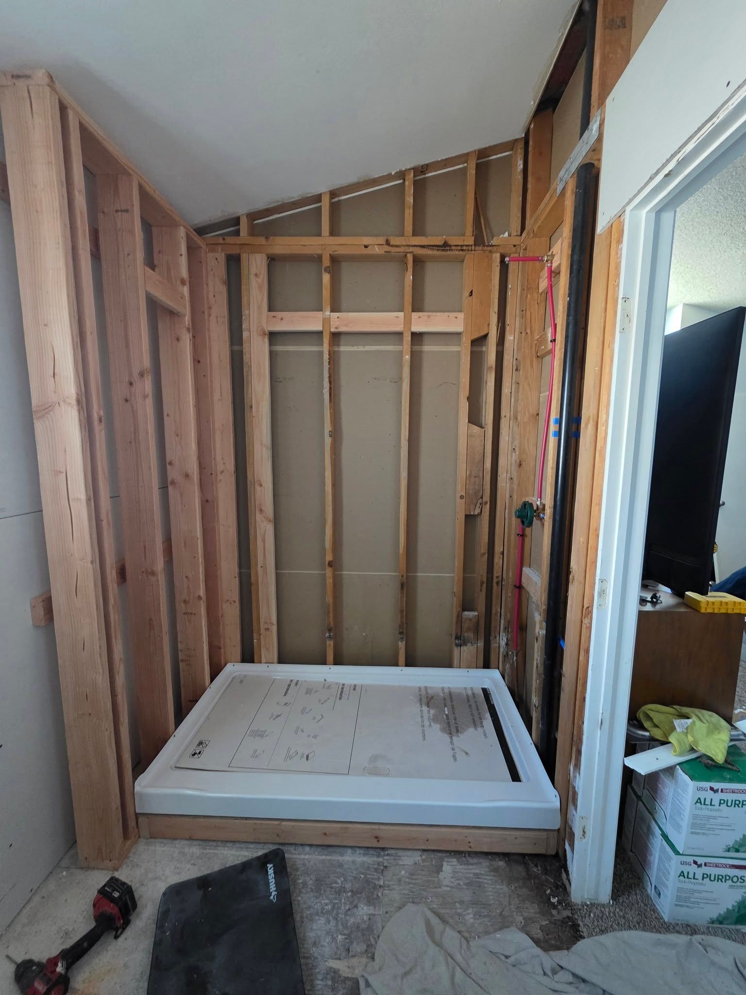 Bathroom under renovation with exposed wall studs, shower pan, and construction tools on the floor