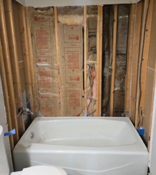Bathtub in a partially remodeled bathroom with exposed wall studs and insulation.