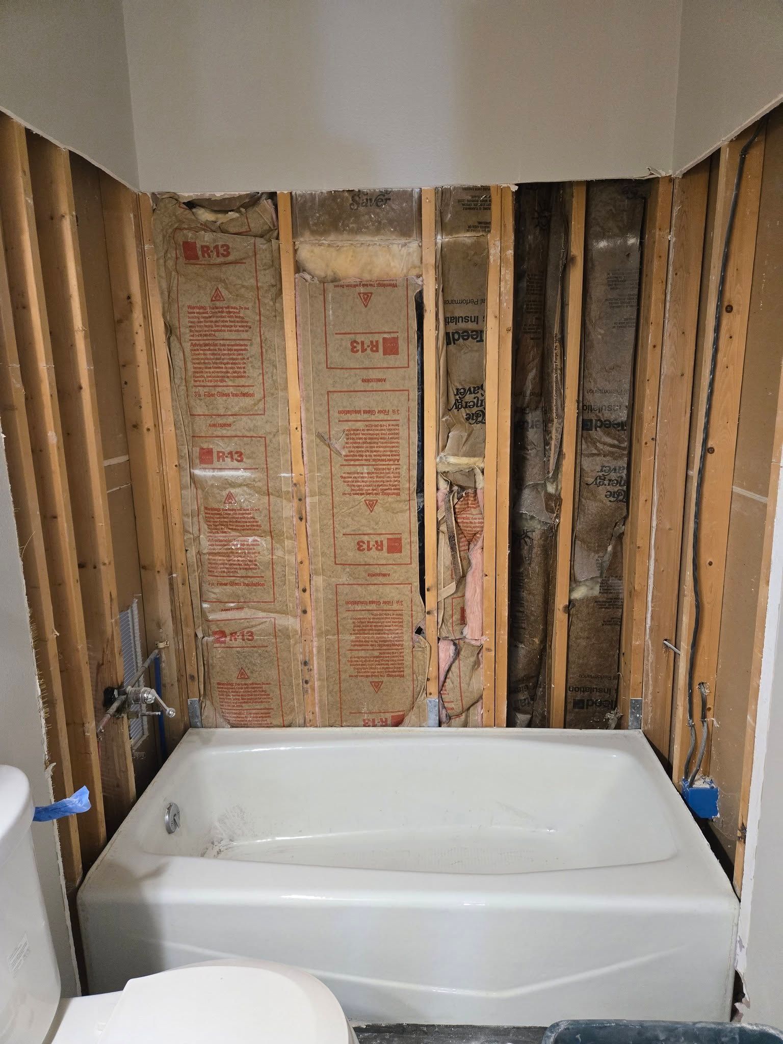 Bathtub in a bathroom under renovation with exposed studs and insulation on the walls