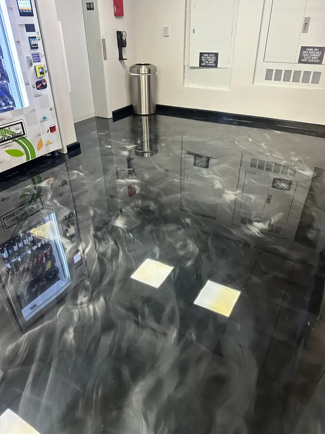 Shiny black and silver epoxy floor in an office setting, reflecting lights and surrounding objects.