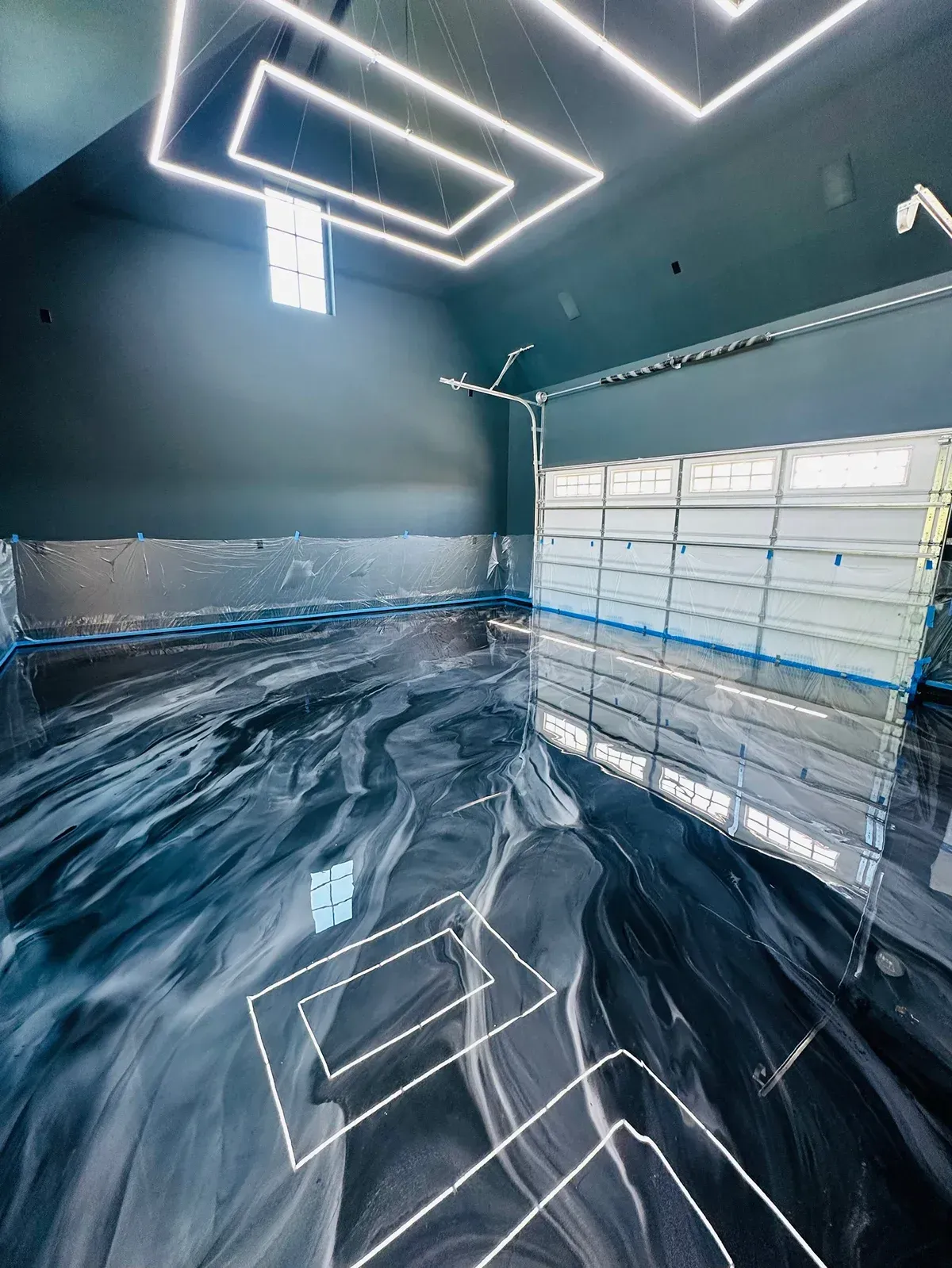 Modern garage with epoxy floor featuring swirling black and gray patterns, glass garage door, and geometric ceiling lights.