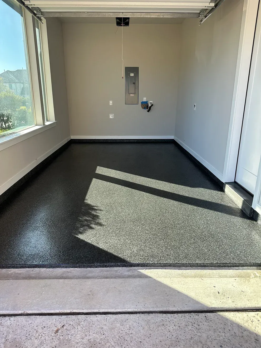 Empty garage with gray speckled epoxy floor, electrical panel, and window.