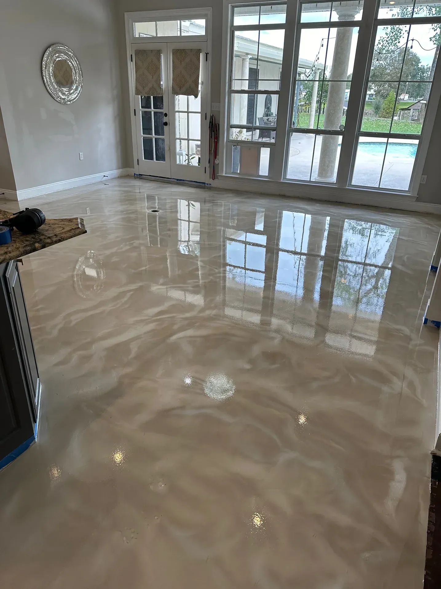 Shiny, metallic-looking epoxy flooring in a light beige color, reflecting sunlight from large windows in a spacious room.