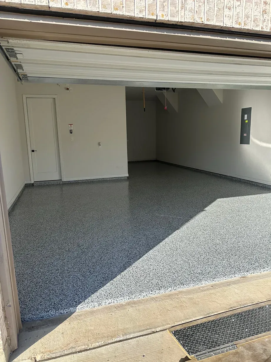 Empty garage interior with a gray epoxy floor. A closed white door is on the left wall.