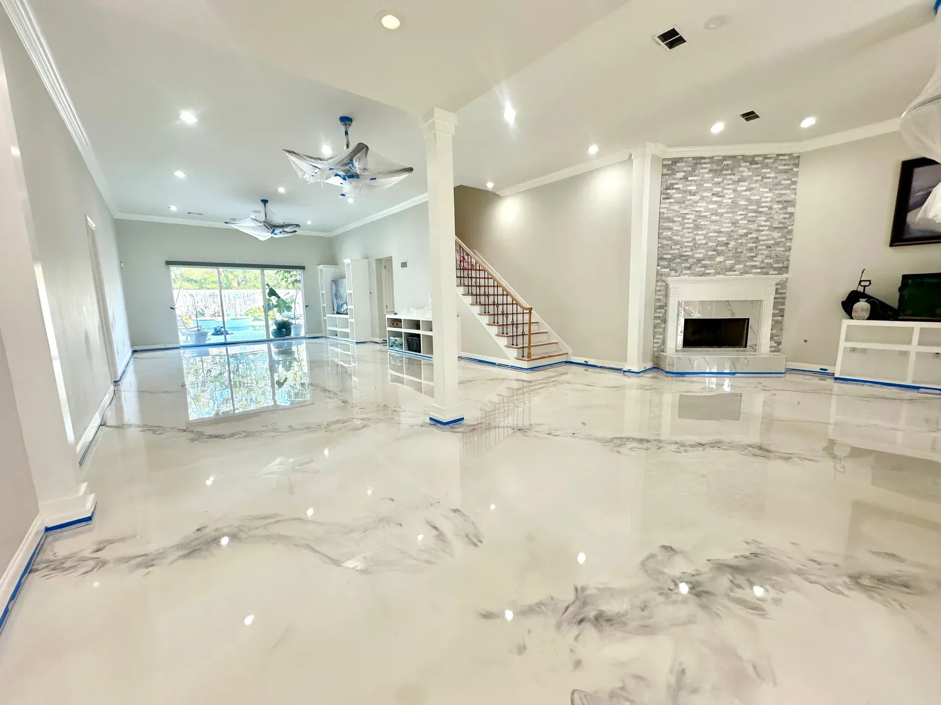 Open living space with white and silver epoxy floor, fireplace, and staircase.