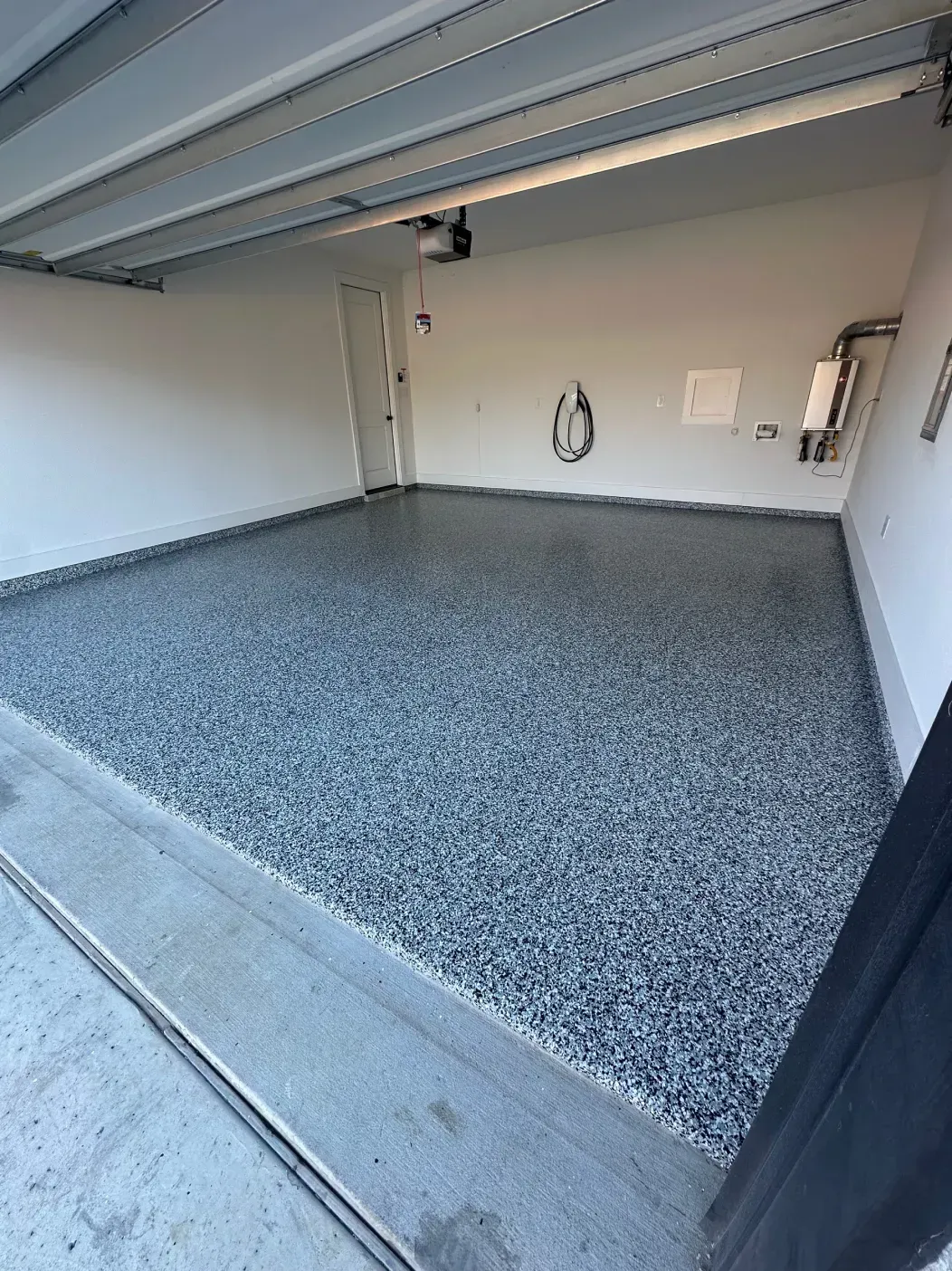 Empty garage with epoxy floor, open garage door. Gray and white speckled floor, white walls.