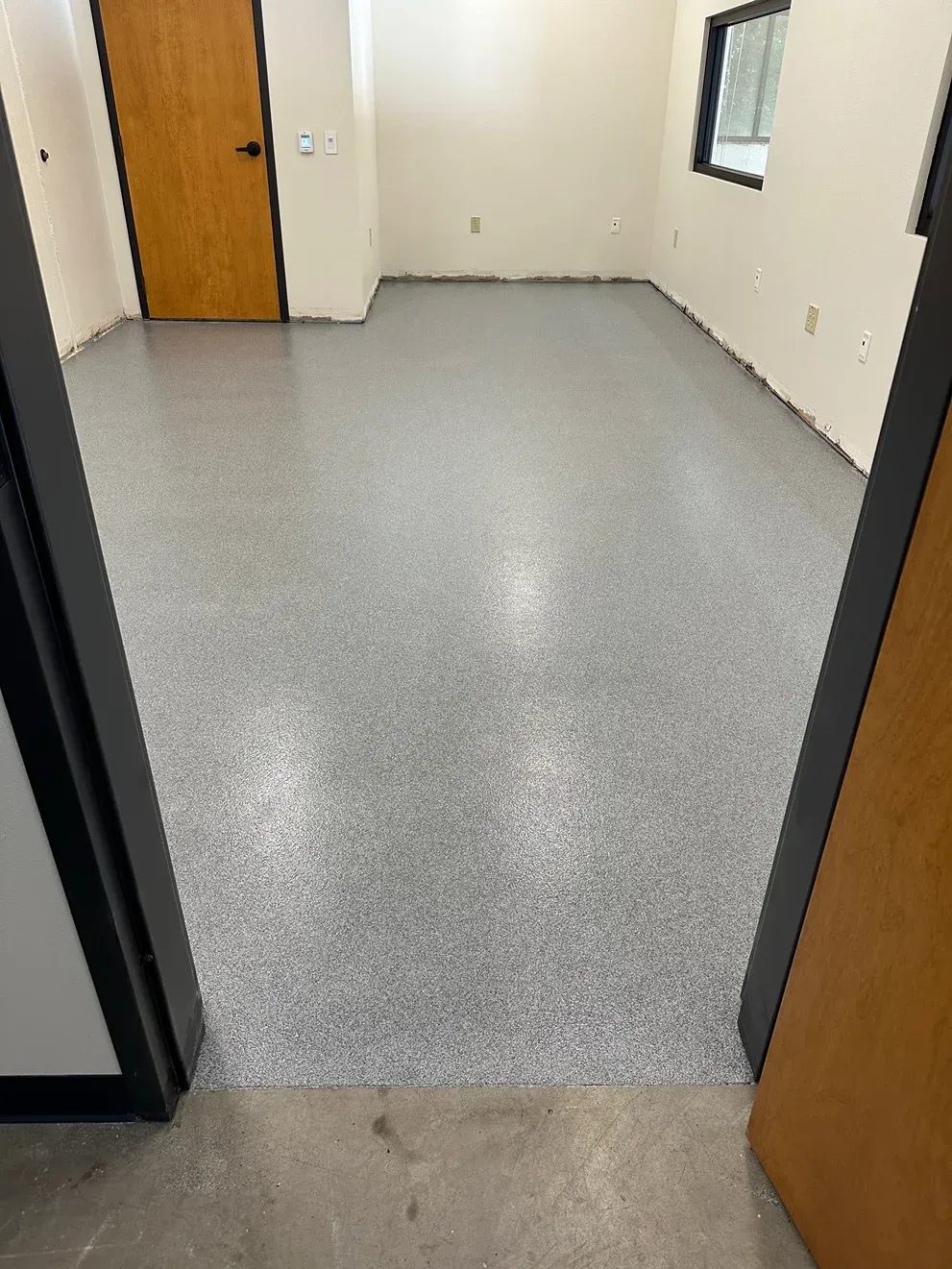 A room with a gray epoxy floor. There is a door in the background and a window to the right.