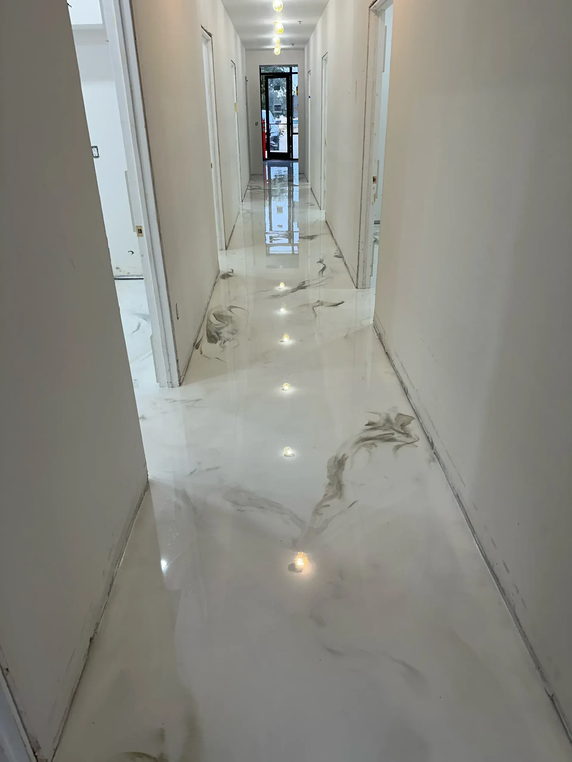 Hallway with shiny white epoxy floor, bright ceiling lights, and white walls.