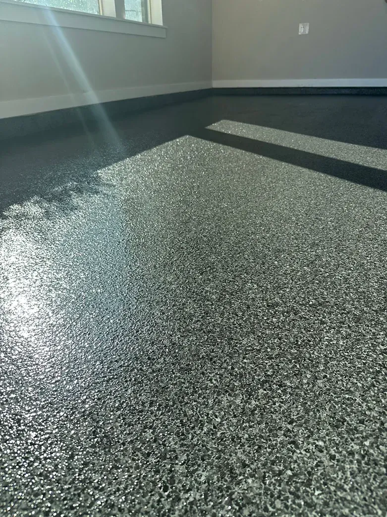 Shiny, speckled gray epoxy floor reflecting light in a room with a window and white walls.