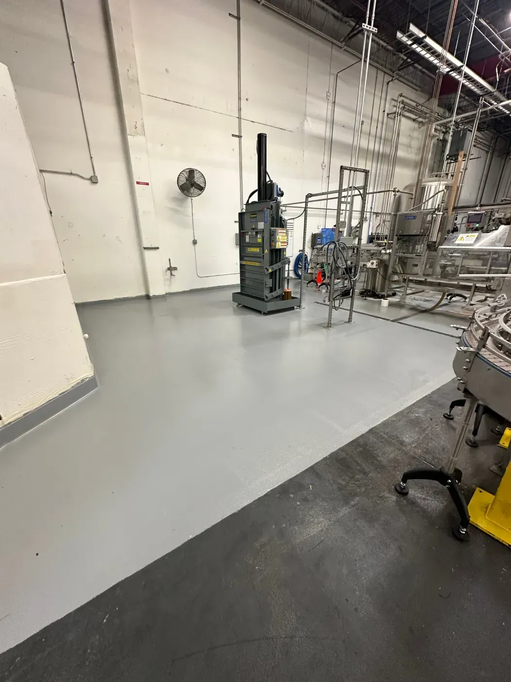 Industrial facility interior with gray and black flooring; machinery and equipment present.