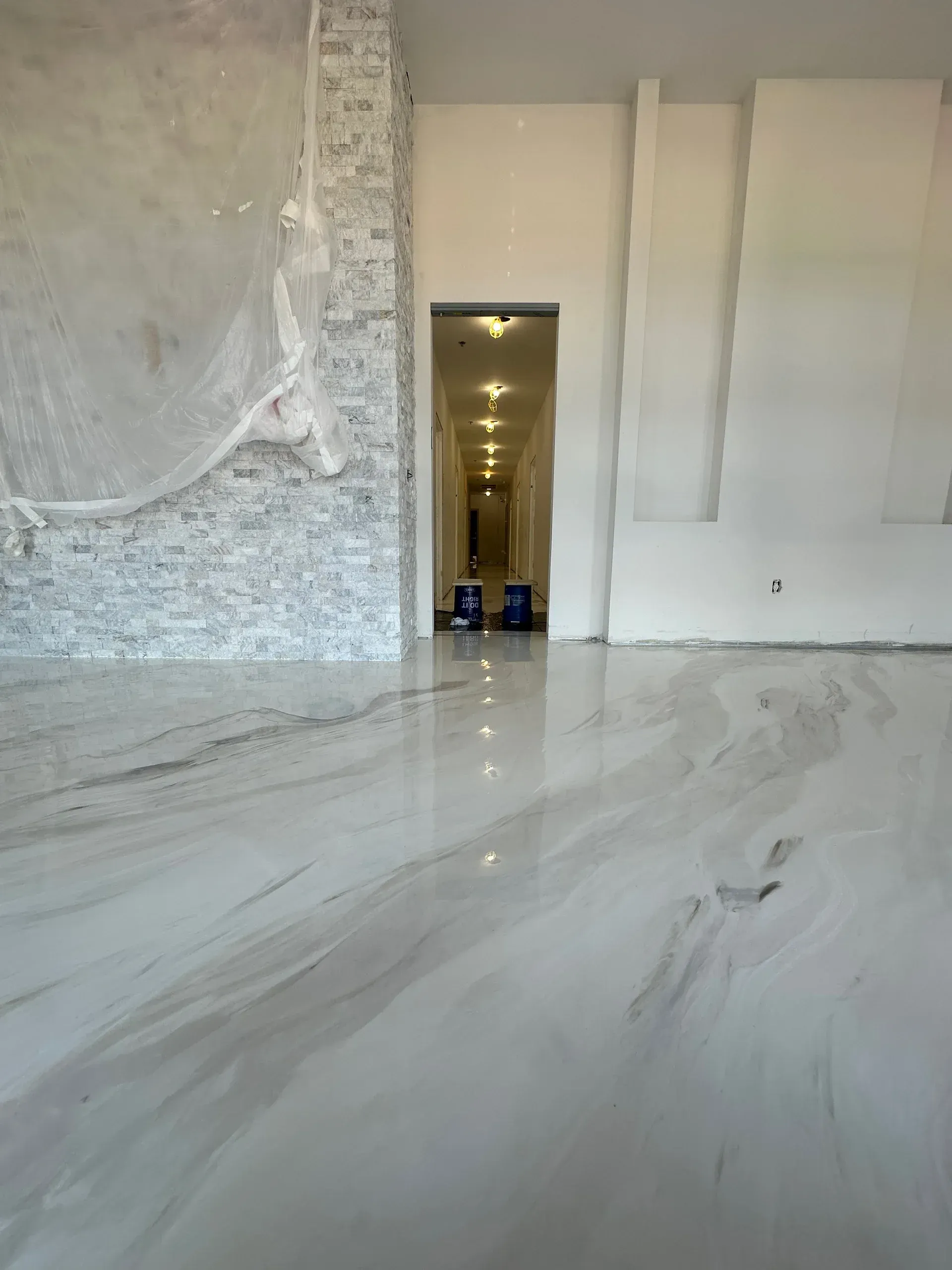 Shiny marble-like epoxy floor in a building under construction.  White walls and a doorway leading to a hallway.